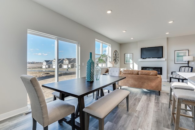 dining space with a glass covered fireplace, recessed lighting, baseboards, and light wood finished floors