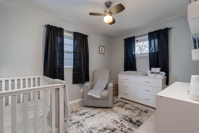 bedroom with a crib, wood finished floors, baseboards, and a ceiling fan