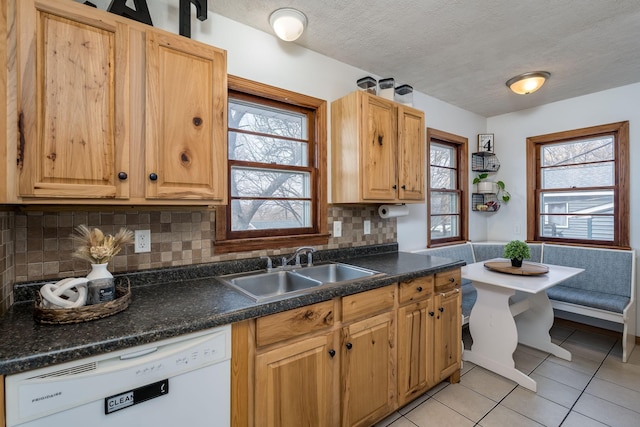 kitchen featuring dark countertops, dishwasher, light tile patterned flooring, a textured ceiling, and a sink