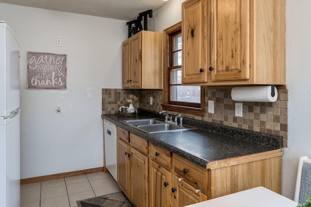 kitchen featuring a sink, backsplash, dark countertops, white appliances, and light tile patterned flooring