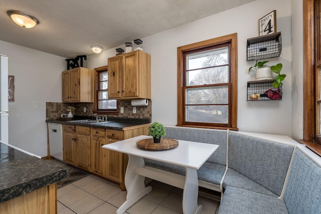 kitchen with a sink, dark countertops, light tile patterned flooring, decorative backsplash, and dishwasher