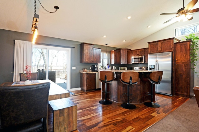 kitchen featuring a breakfast bar, appliances with stainless steel finishes, light countertops, lofted ceiling, and dark wood-style flooring