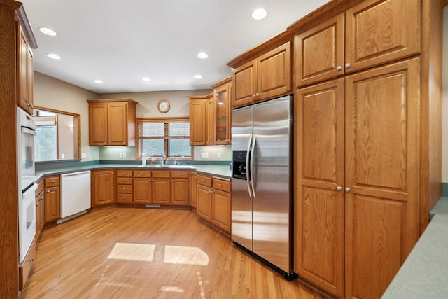 kitchen with light wood-style flooring, a sink, recessed lighting, white appliances, and brown cabinetry