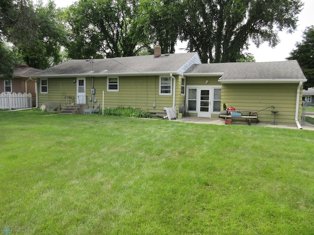 rear view of house featuring fence, roof with shingles, a lawn, a chimney, and a patio area