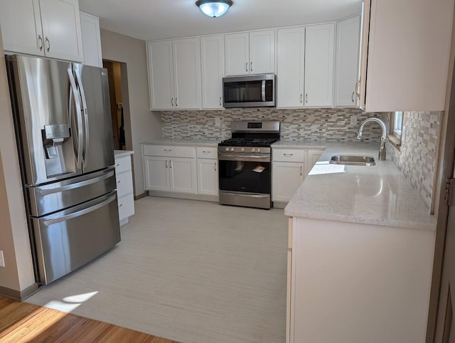 kitchen with backsplash, light stone counters, stainless steel appliances, white cabinetry, and a sink