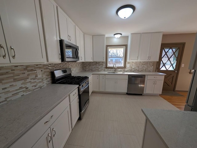 kitchen featuring backsplash, white cabinets, stainless steel appliances, and a sink