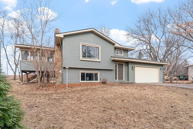 split level home featuring stairway, an attached garage, a chimney, and driveway