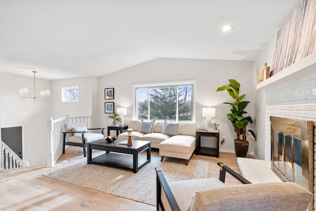 living room with a notable chandelier, plenty of natural light, light wood-style flooring, and a brick fireplace