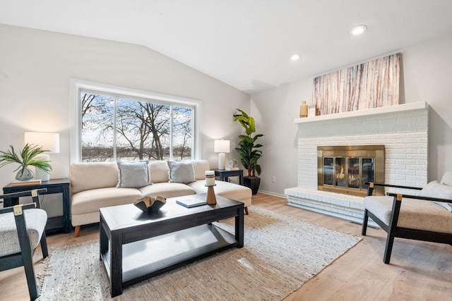 living room featuring baseboards, light wood finished floors, lofted ceiling, recessed lighting, and a brick fireplace