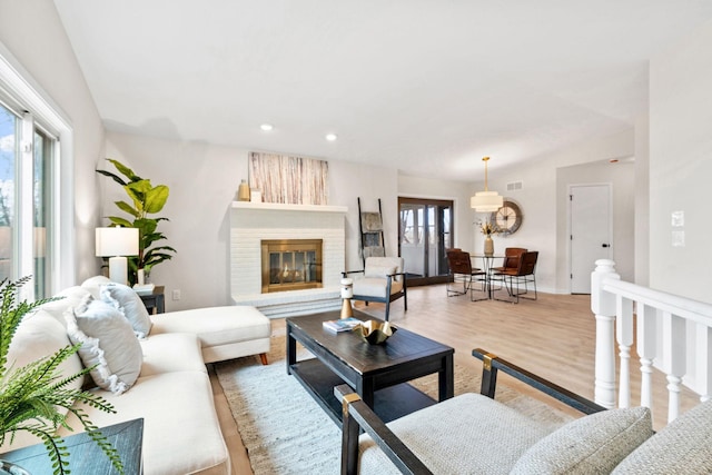 living room with recessed lighting, plenty of natural light, light wood-style flooring, and a glass covered fireplace