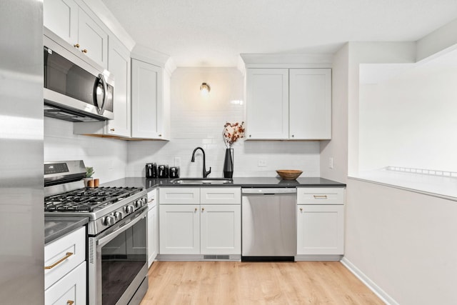 kitchen featuring light wood-style flooring, a sink, stainless steel appliances, white cabinets, and dark countertops