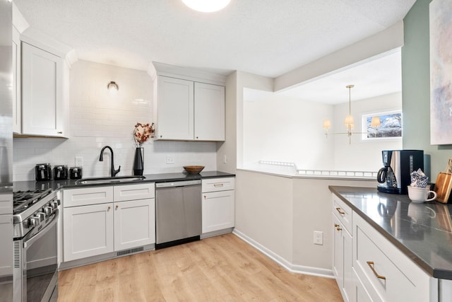 kitchen with dark countertops, backsplash, light wood-style floors, stainless steel appliances, and a sink