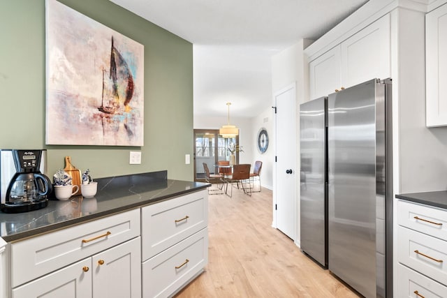 kitchen featuring light wood-style flooring, dark countertops, white cabinets, and freestanding refrigerator