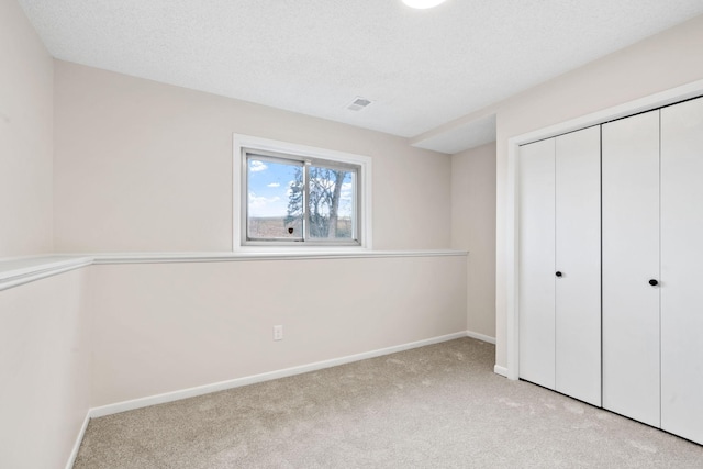 unfurnished bedroom with visible vents, a textured ceiling, a closet, carpet floors, and baseboards