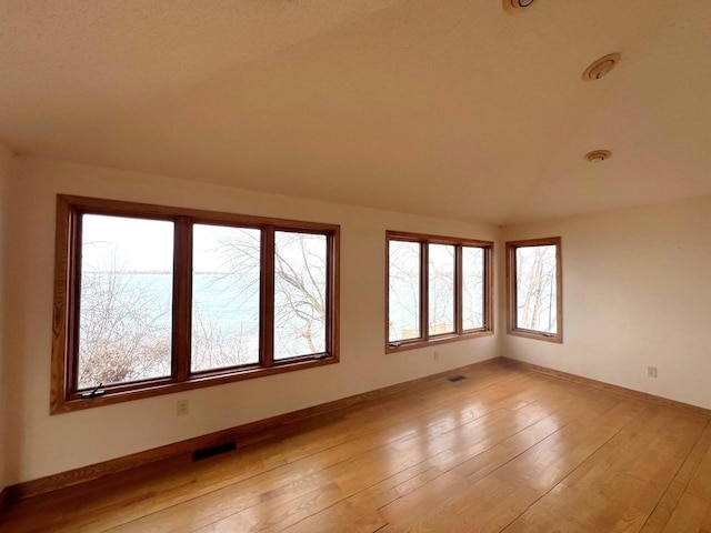 empty room with vaulted ceiling, visible vents, baseboards, and light wood finished floors