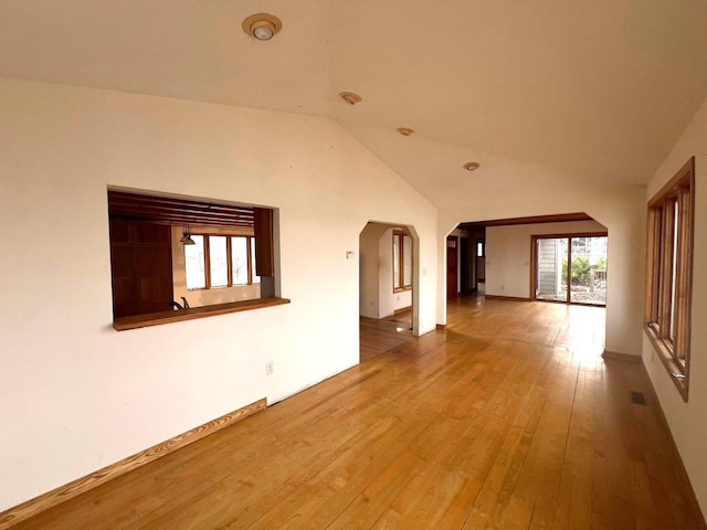 empty room with visible vents, arched walkways, lofted ceiling, and hardwood / wood-style flooring