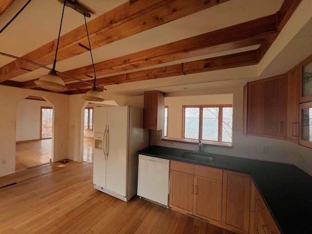 kitchen featuring dark countertops, beamed ceiling, light wood-style flooring, white appliances, and a sink