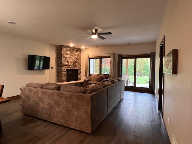 living room featuring a stone fireplace, a ceiling fan, and dark wood-style flooring