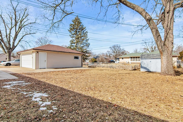 view of yard featuring driveway, a detached garage, an outdoor structure, and fence