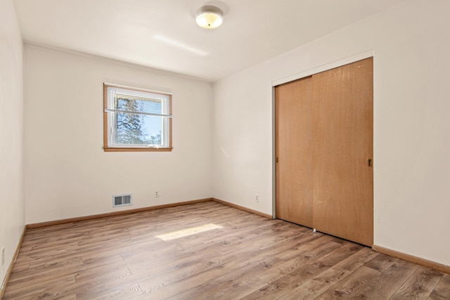 unfurnished bedroom with wood finished floors, visible vents, a closet, and baseboards