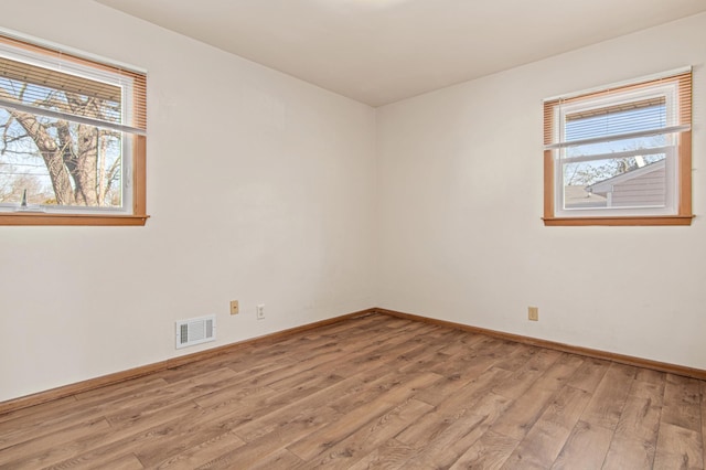 spare room with light wood finished floors, visible vents, and baseboards