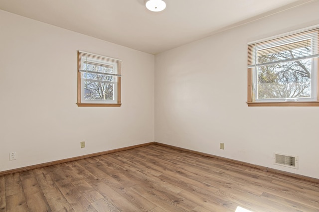 unfurnished room with light wood finished floors, visible vents, and baseboards