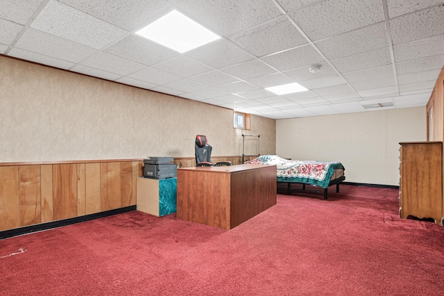 unfurnished bedroom with wooden walls, carpet, and a drop ceiling