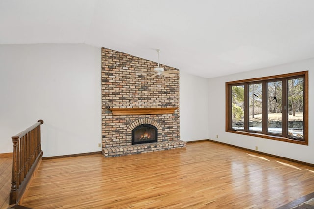 unfurnished living room featuring wood finished floors, a fireplace, baseboards, ceiling fan, and vaulted ceiling