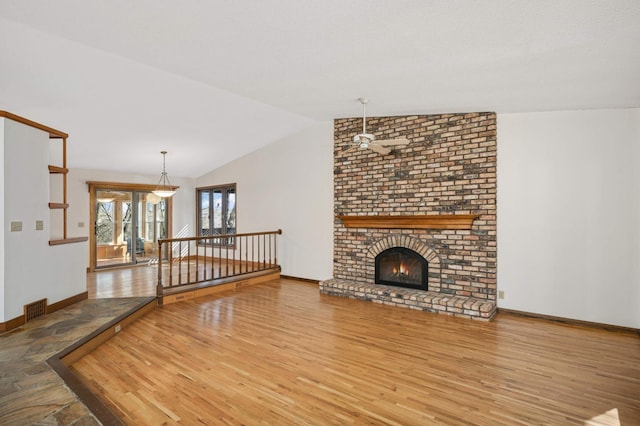 unfurnished living room with wood finished floors, visible vents, baseboards, lofted ceiling, and a brick fireplace