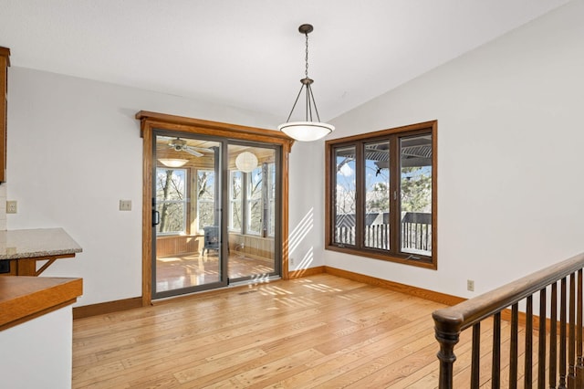 unfurnished dining area with baseboards, lofted ceiling, a healthy amount of sunlight, and light wood finished floors