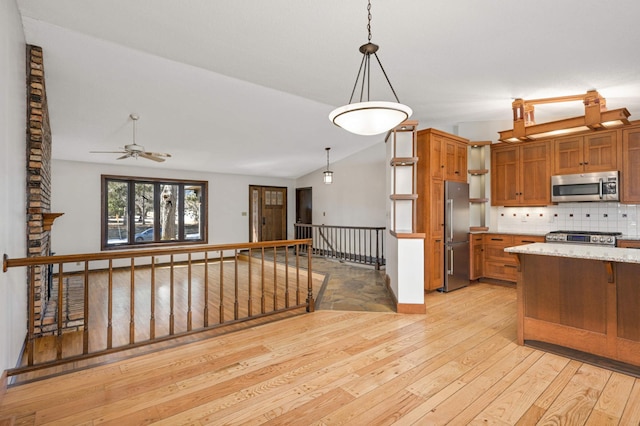 kitchen featuring light wood finished floors, backsplash, lofted ceiling, appliances with stainless steel finishes, and brown cabinetry