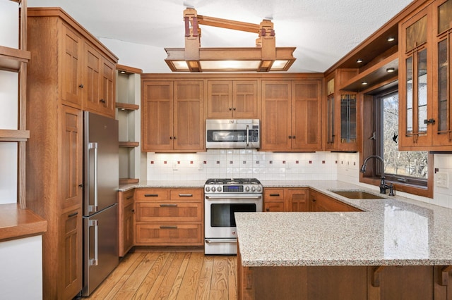 kitchen with a sink, brown cabinets, a peninsula, stainless steel appliances, and open shelves