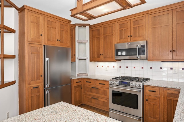 kitchen with brown cabinetry, backsplash, appliances with stainless steel finishes, and light stone counters