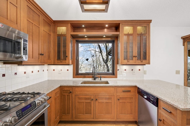 kitchen with light stone counters, brown cabinetry, appliances with stainless steel finishes, and a sink