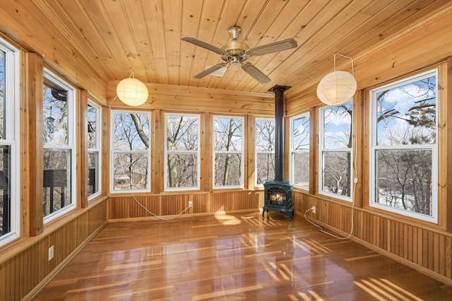 unfurnished sunroom featuring plenty of natural light, wood ceiling, ceiling fan, and a wood stove