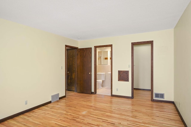 spare room featuring light wood finished floors, visible vents, and baseboards