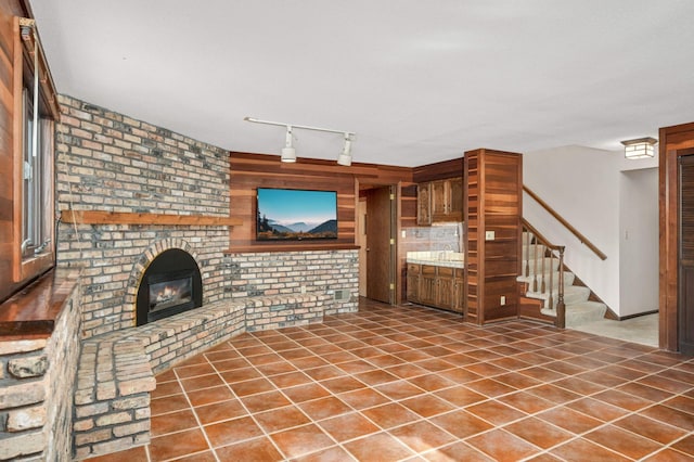 unfurnished living room with tile patterned flooring, stairway, a fireplace, and track lighting