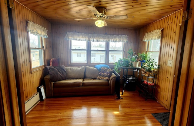 living area with light wood-style flooring, wooden walls, wood ceiling, and a baseboard radiator