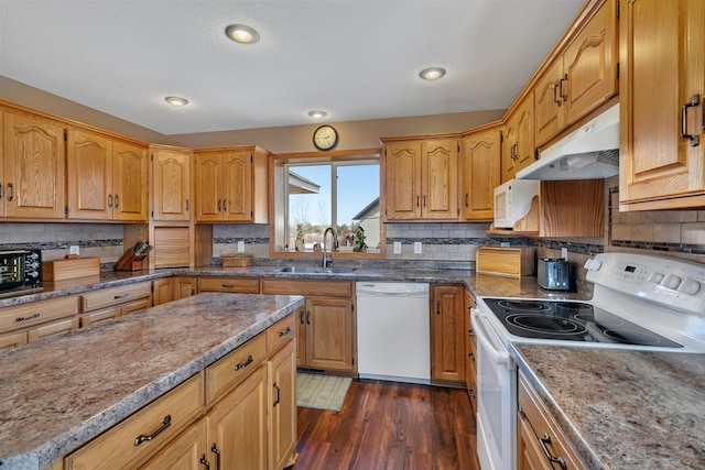 kitchen with tasteful backsplash, dark wood-type flooring, under cabinet range hood, white appliances, and a sink