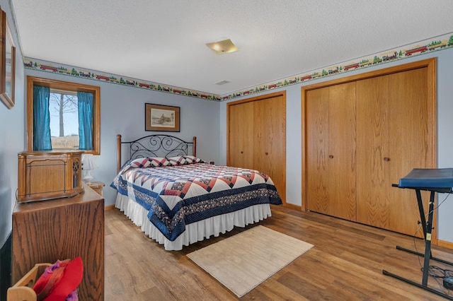 bedroom featuring baseboards, two closets, light wood-style flooring, and a textured ceiling