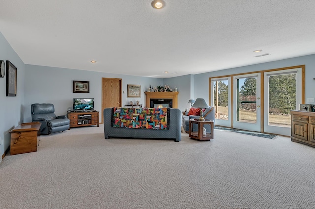 carpeted living room featuring visible vents, recessed lighting, a textured ceiling, and a glass covered fireplace