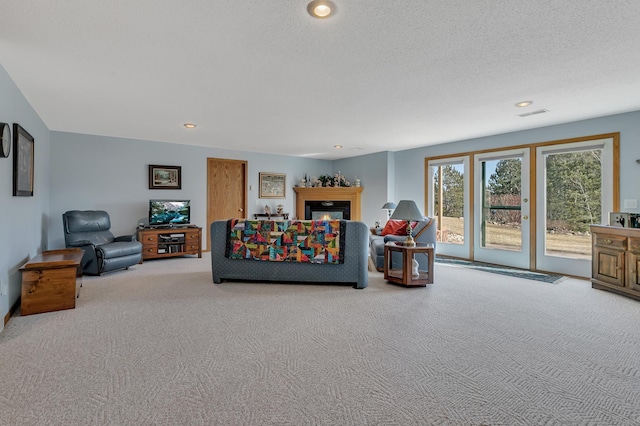 living area with a textured ceiling, a glass covered fireplace, visible vents, recessed lighting, and carpet floors