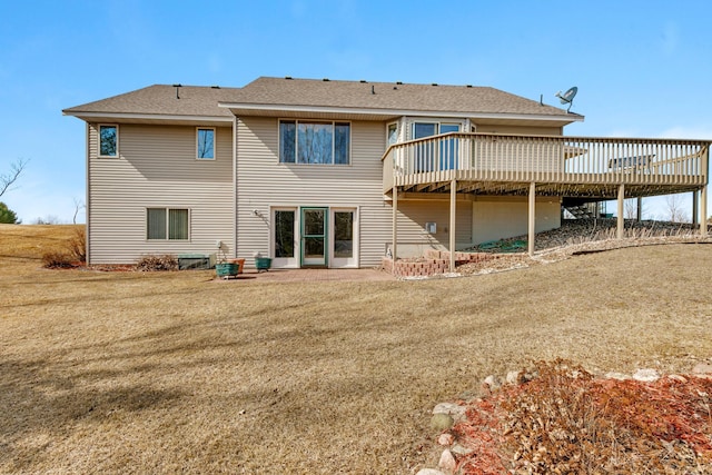back of property featuring a deck, a lawn, and roof with shingles