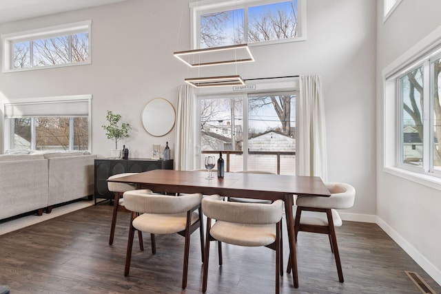 dining space with a wealth of natural light, dark wood-type flooring, and a high ceiling