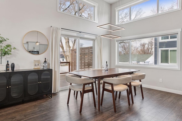 dining room with dark wood finished floors, baseboards, and a towering ceiling