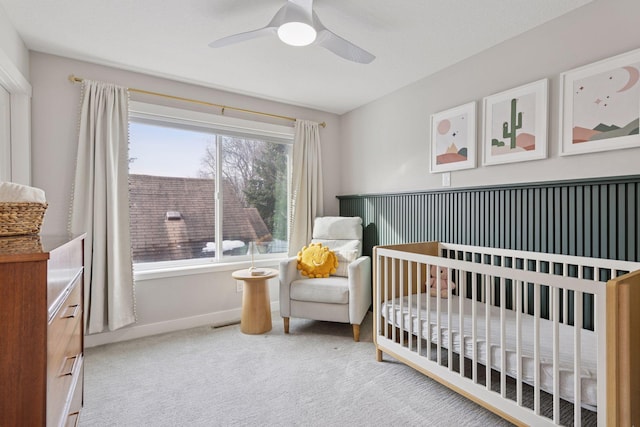 bedroom featuring a crib, carpet flooring, a ceiling fan, and baseboards