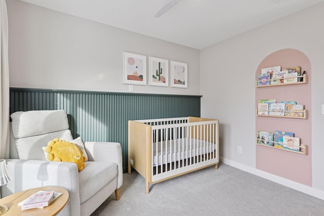 carpeted bedroom with baseboards, a crib, and a ceiling fan