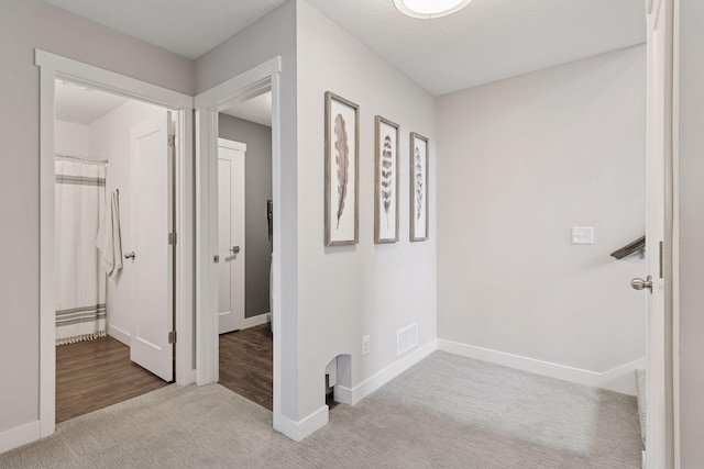 hall with visible vents, a textured ceiling, baseboards, and carpet floors