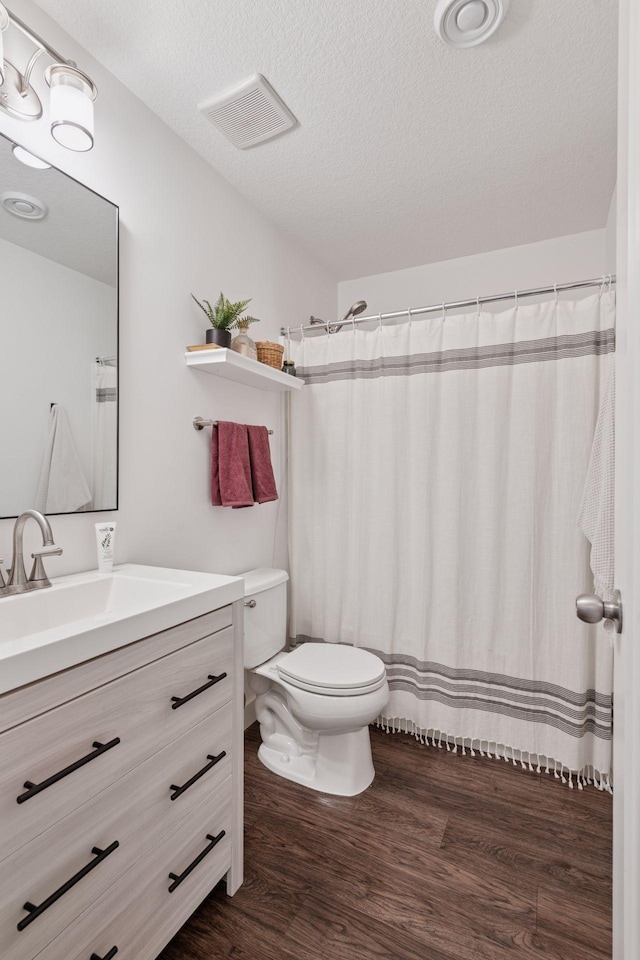 bathroom with visible vents, toilet, a textured ceiling, wood finished floors, and vanity