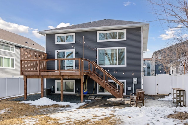 snow covered rear of property featuring a deck, fence, an outdoor fire pit, central AC unit, and stairs